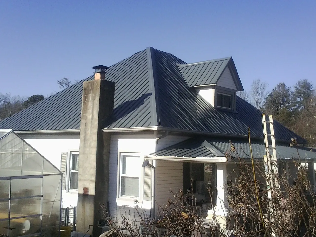 Dark blue standing seam metal roof on a white farmhouse with dormer — Slate & Tile Roof Repair by Roofing Brothers in Zapata