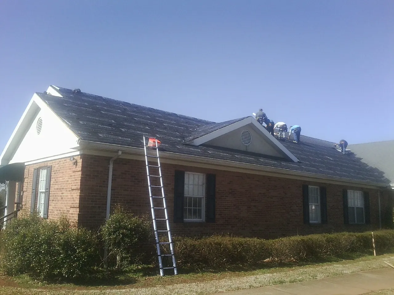 Crew tearing shingles off a brick ranch roof with a ladder set — Emergency Roof Repair work by our crew in Zapata