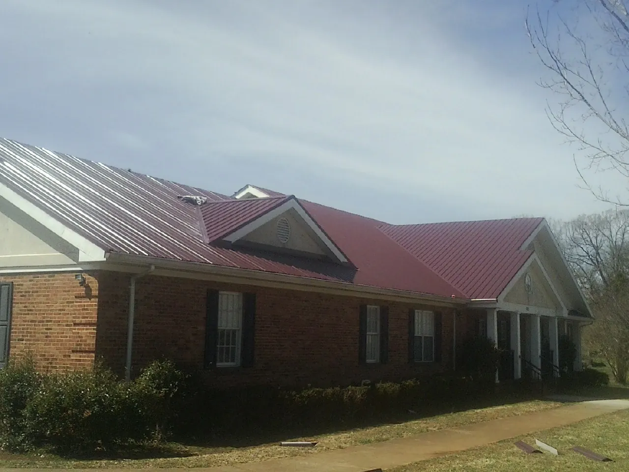 Red metal roof with gabled entries on a long brick building, from a Hail Damage Roof Repair job in Zapata