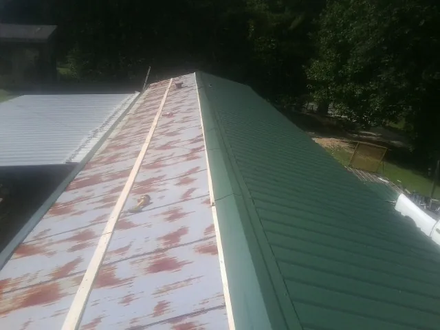 Old rusted panels beside newly installed green metal roofing — Wind Damage Roof Repair by Roofing Brothers in Zapata
