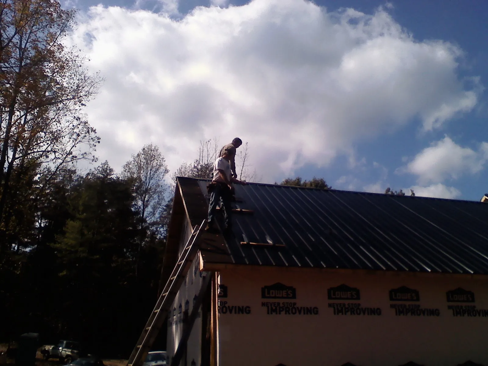 Roofer fastening dark metal panels high against a cloudy sky, from a Roof Inspection job in Zapata